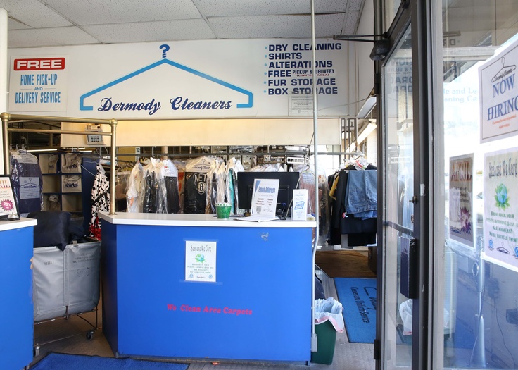 A dry cleaner's counter with a card machine and its printed slip beside the ticket book, a rail of bagged clothes behind.