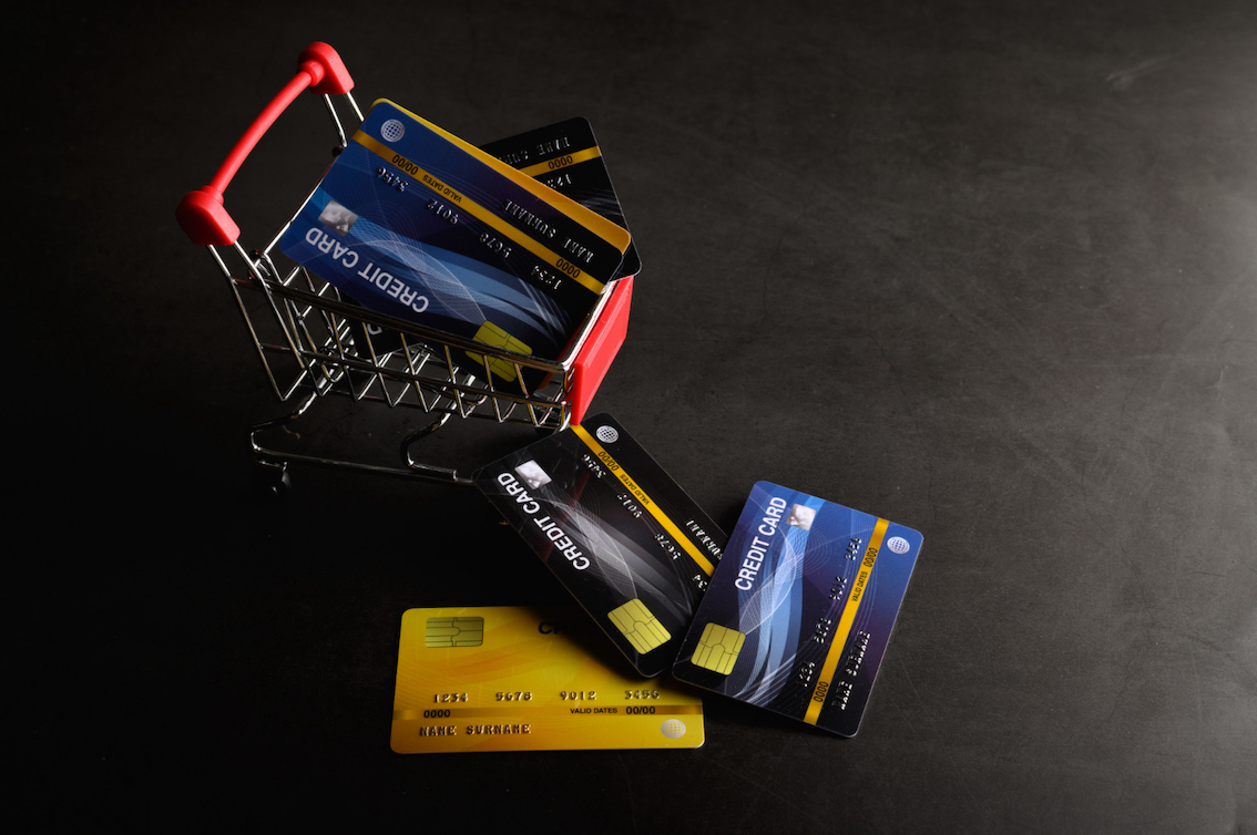 Five business credit cards laid on a desk beside a laptop showing a card statement and a fuel slip.