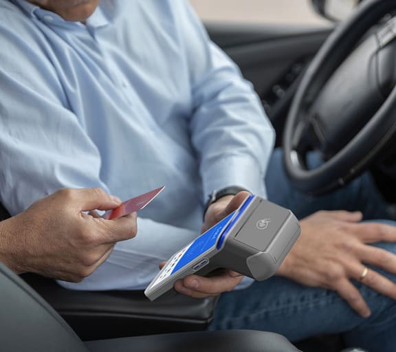 A passenger tapping a card machine held by a taxi driver at the window, in daylight.