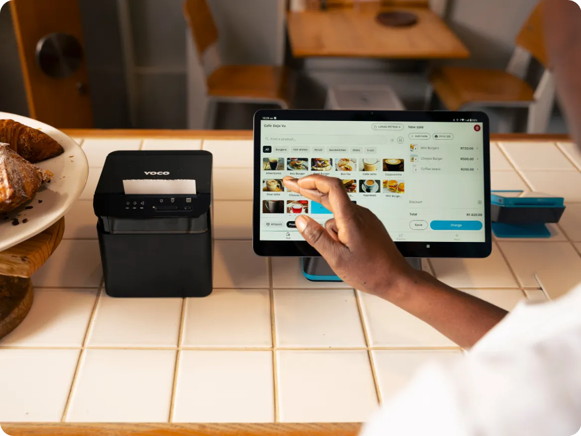 A waiter holding a card machine at a restaurant table, with a printed bill beside the plates.