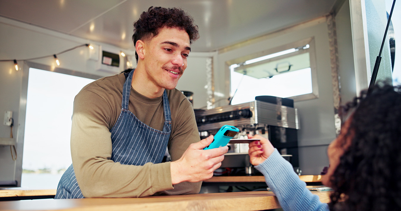 A food-truck vendor in an apron holds a card machine out at the hatch while a customer pays by card